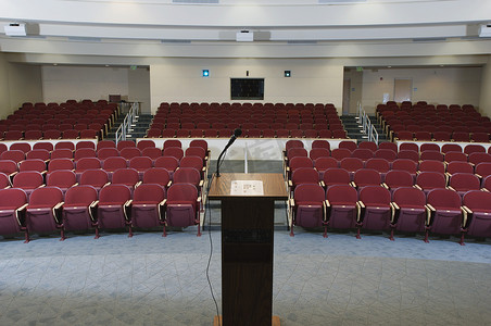 剧场座位摄影照片_在一个空荡荡的会议礼堂里，按顺序排列着红色椅子和讲台