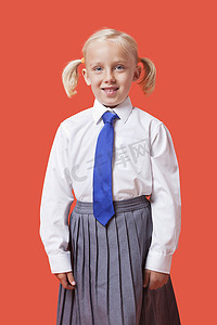 校服女孩摄影照片_橙色背景中穿着校服的快乐小女孩的画像