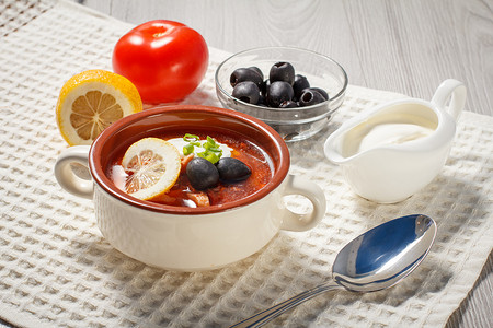 酸乳摄影照片_在陶瓷汤碗中用肉、土豆、西红柿、柠檬、黑橄榄和酸奶油汤盐麦芽汁。
