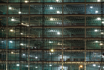 夜间大型建筑工地的全框架视图，由带有大梁和施工升降机的明亮工作灯照亮