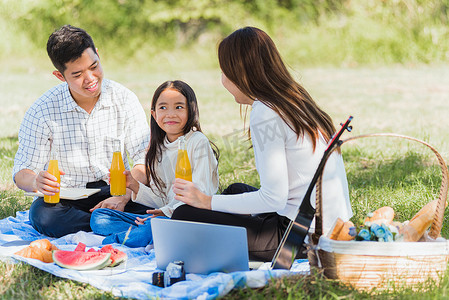 快乐的家庭坐在野餐毯上享受户外乐趣，喝着玻璃瓶里的橙汁
