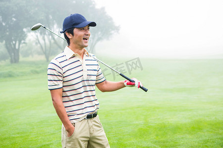 微笑的高尔夫球手站着，拿着他的球杆