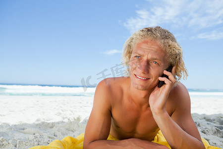 年轻的金发男子躺在沙滩上打电话