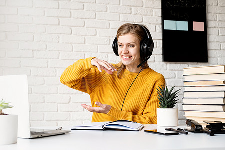戴着黑色耳机微笑的年轻女性使用笔记本电脑在视频聊天中聊天在线学习