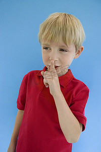 男性嘴唇摄影照片_可爱的小男孩，手指放在嘴唇上，与蓝色背景隔离