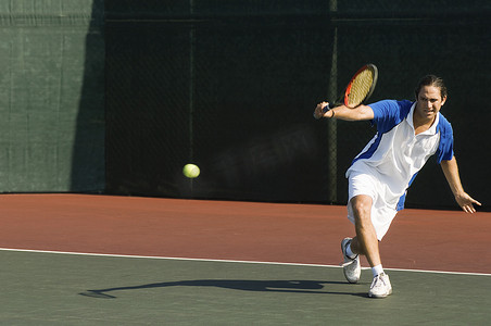 网球击球摄影照片_一名男子网球运动员在网球场上反手击球的全长