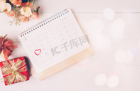 日历和花与备忘录 2 月 14 日情人节在桌子上有模糊的散景背景，提醒爱情惊喜，浪漫和甜蜜，庆祝和装饰，顶视图，假日概念。
