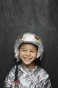 儿童宇航服摄影照片_一个穿着铝箔宇航服的可爱小男孩在黑色背景下微笑的肖像