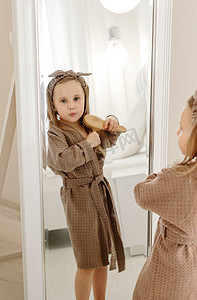 大外套摄影照片_一个穿棕色外套的女孩透过大镜子看着镜头
