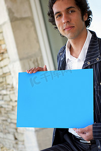 海报蓝色海报摄影照片_男人拿着蓝色海报站在屋外