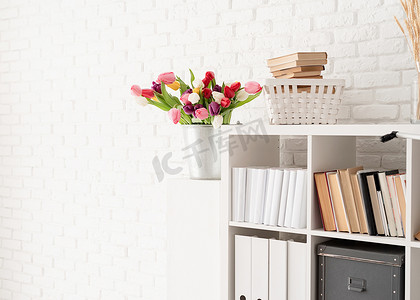 白砖墙背景下书架旁的一桶郁金香花