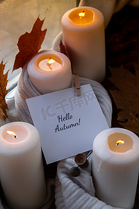 万圣节氛围摄影照片_HELLO AUTUMN 文字贺卡概念 在窗台上舒适的家中庆祝秋季假期 Hygge 审美氛围 秋叶香料和蜡烛在温暖的黄色灯光下的针织白色毛衣上。
