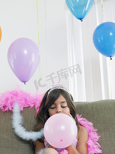 坐在沙发上吹气球的小女孩