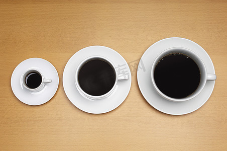 根据尺寸在木质表面上排列的三个咖啡杯的高角度视图