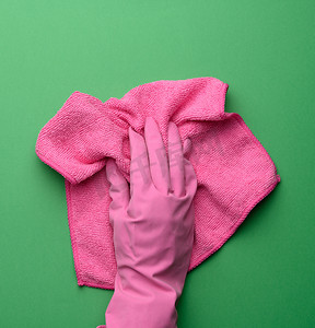 粉色橡胶手套中的女手拿着紫色背景上的粉色清洁抹布