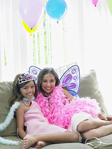 初等摄影照片_两个穿着派对服装坐在沙发上的快乐年轻女孩的画像