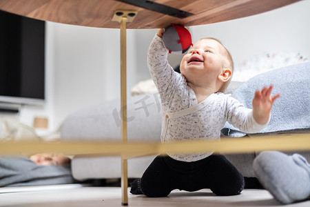吊球摄影照片_可爱的男婴在家里的客厅桌子旁玩吊球、爬行和站起来。