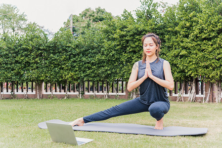 在户外练习瑜伽的在线视频培训中使用笔记本电脑的女性