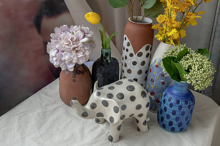 白色纹理桌布上的大象形陶瓷和手工制作的多种不同的陶瓷波尔卡圆点花瓶。