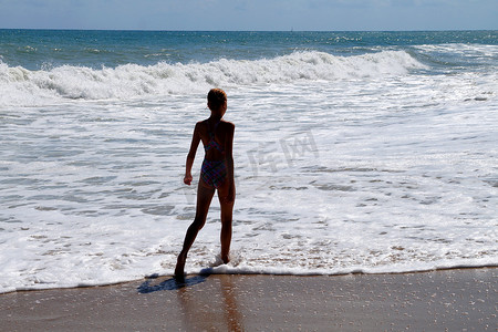 阳光明媚的日子里，少女独自走在空荡荡的海边，后视