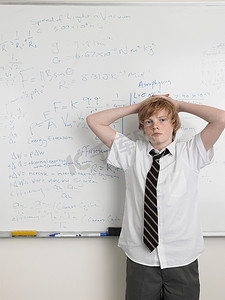 冷漠的目光摄影照片_一名年轻男学生手放在头上站在教室里的肖像
