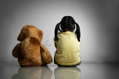 自闭症患者摄影照片_带着泰迪熊的小女孩坐在空房间的地板上。
