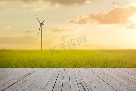 在绿色稻田的风力涡轮机反对与板条木头前景的日落背景。
