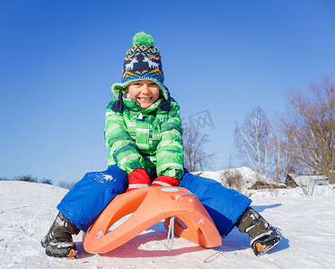 在冬季公园玩雪橇的小男孩