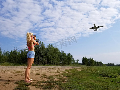一头长发的金发女孩在多云的天空背景下拍下一架飞机飞过她的照片