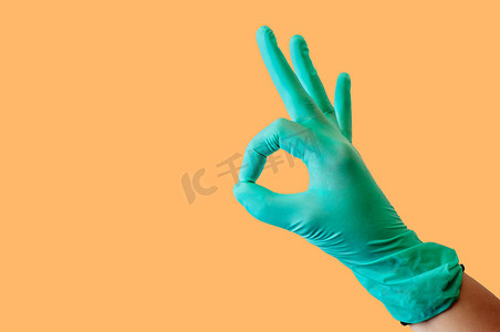 女性手上的蓝色乳胶医用手套，在浅橙色背景下显示出良好的性格。