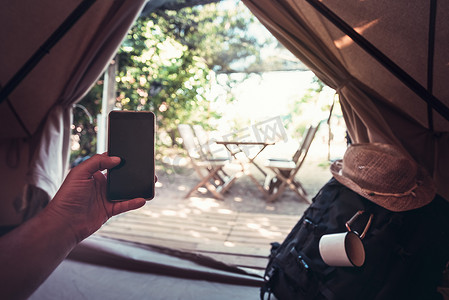 流浪的人摄影照片_在野营帐篷里拿着电话的人的手