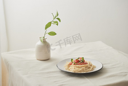 食物、白盘中的肉酱意大利面和准备好的白色桌子上的一瓶植物
