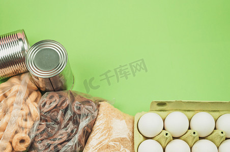 食物捐赠，鸡蛋的顶视图，罐头食品，意大利面，绿色背景中突显的饼干。