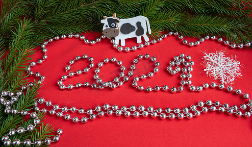 2021牛牛牛摄影照片_“云杉树枝，红色背景中的白牛和 2021 年的数字，上面镶着银珠。新年的概念”