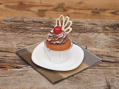 带巧克力奶油和樱桃旧木背景的纸杯蛋糕