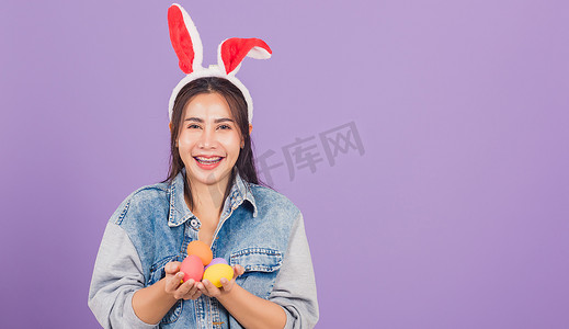 戴着兔耳和牛仔布微笑的女人手上拿着彩色复活节彩蛋礼物