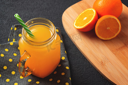 桌子上的罐子摄影照片_用橙子新鲜制作的柑橘汁，放在罐子里，杯子里放着灰色桌子上的吸管