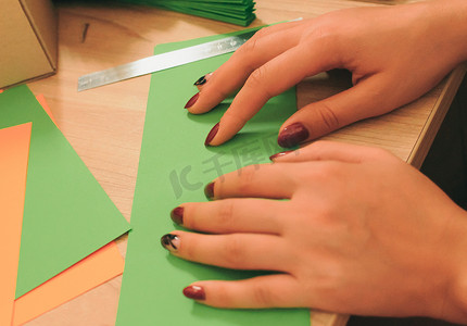 在前景中，一个女孩在木桌上准备折纸扇、彩色纸片和剪刀。