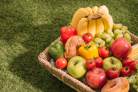 草地上的野餐毯上放着新鲜健康的热带水果，上面放着葡萄、苹果、葡萄柚、橙子和香蕉