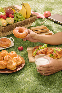 野餐柳条篮，里面有食物、面包、水果和橙汁，放在红色和白色的格子布上，背景是绿色。