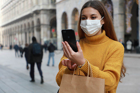 城市街道上使用智能手机应用程序戴外科口罩的购物女性