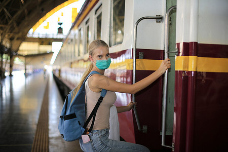 戴着面罩的年轻女子在老式火车上等候，在泰国曼谷的车站站台上放松而无忧无虑，然后才赶上火车。