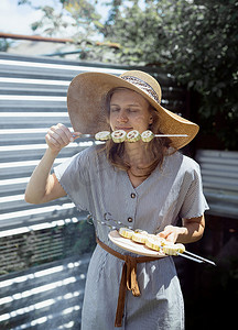 闻肉味道摄影照片_戴着夏日帽子的年轻女人在户外闻着烤蔬菜的味道
