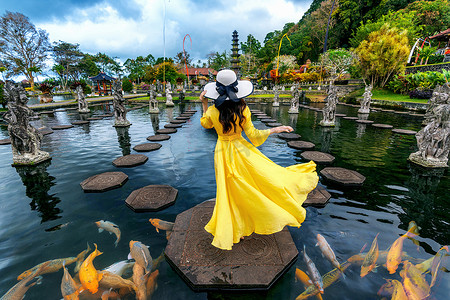 在印度尼西亚巴厘岛的 Tirta Gangga 水宫，女人站在池塘里，身边有五颜六色的鱼。