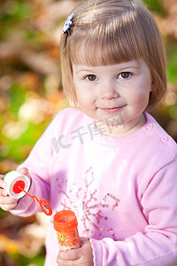 美丽的小女孩在秋天的森林里吹泡泡