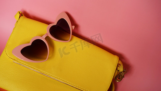 粉红色背景中的黄色包和心形太阳镜