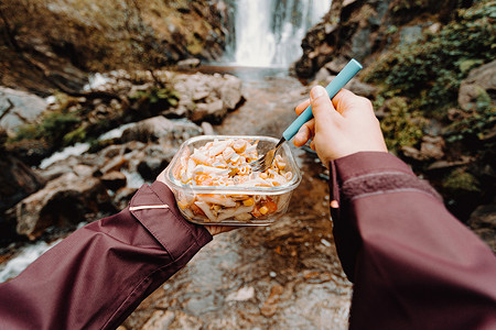 一位女性徒步旅行者在瀑布前吃饭的视角照片