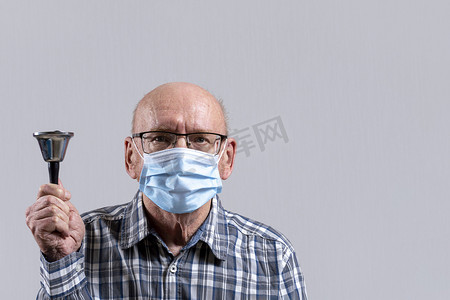 kfc老头摄影照片_秃头老头戴着眼镜，戴着医用面具，手里拿着铃铛。