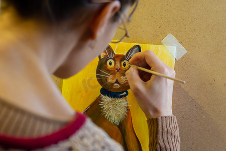 艺术家用丙烯酸颜料在画架上画了一幅猫的图画，从艺术家的背影看