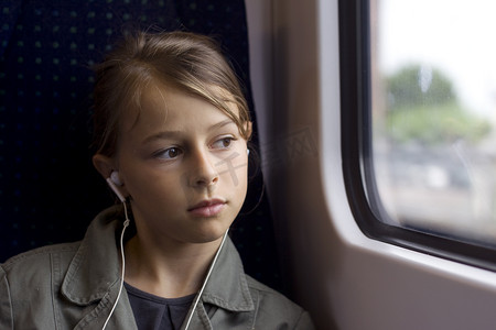火车外摄影照片_戴耳机的女孩在火车或公共汽车上从窗外望去